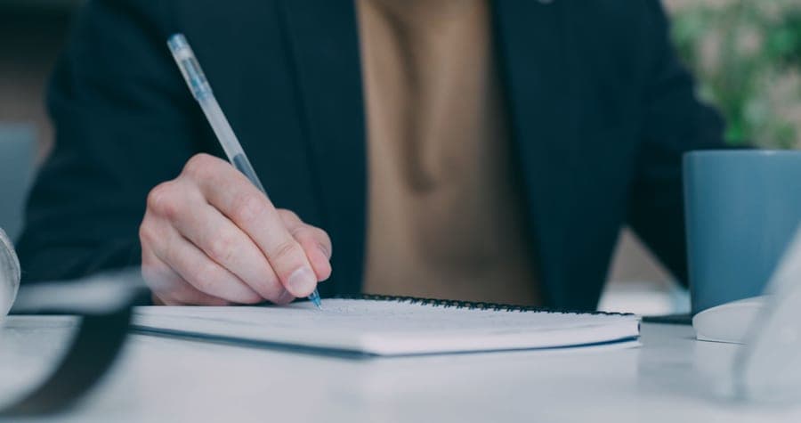 A person reading a manual and taking notes at a desk